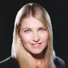 happy woman with long blonde hair and blue eyes, smiling on dark background, elegant attire with earrings and necklace