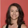 smiling woman with shoulder-length brown hair against a red background, portrait of woman in a sleeveless black top