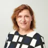 smiling woman with wavy brown hair wearing a geometric patterned blouse, neutral background in a professional portrait setting