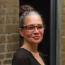 woman with glasses and bun hairstyle smiling against a brick wall, portrait of a confident woman in casual attire