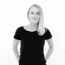woman with long blonde hair in black shirt against white background, smiling expression highlighting casual style and confidence