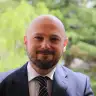 businessman in tailored suit, smiling outdoors with green foliage background, professional portrait with blurred nature backdrop