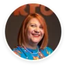 smiling woman with short red hair wearing a colorful patterned blouse and a pearl necklace against a dark background, portrait of cheerful woman in front of lettering