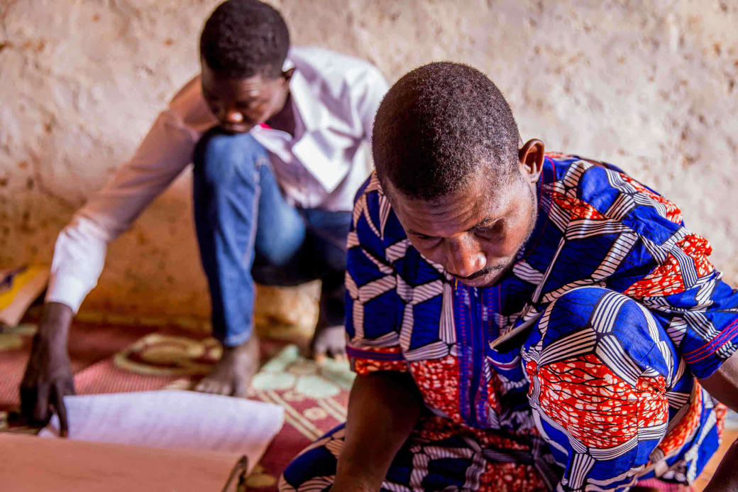 Twee mannen zoeken hun naam op de stemlijsten. Stemgerechtigden moeten verplicht hun stemkaart afhalen bij de chef du quartier.