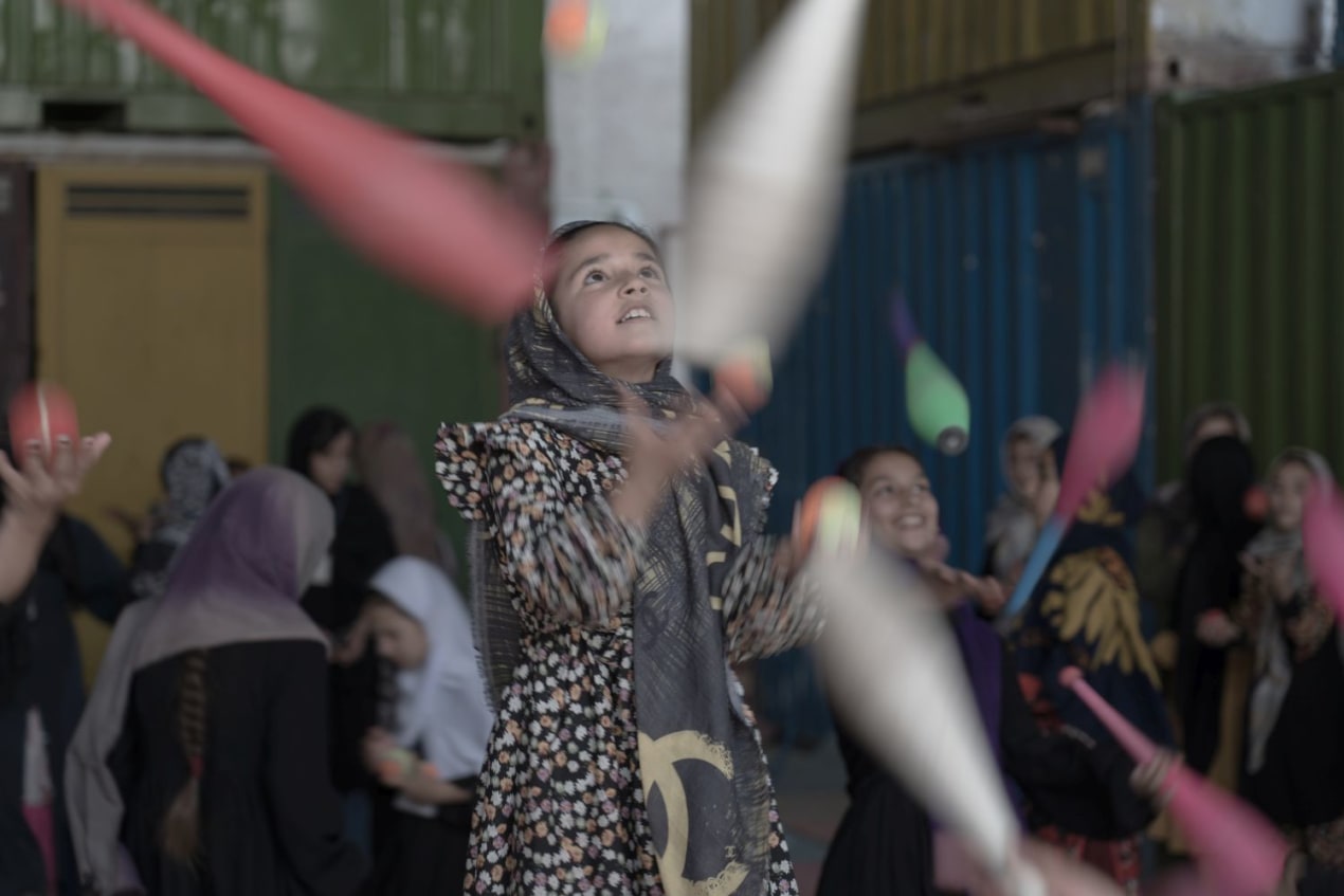 De meisjes jongleren staand op een skippybal met ballen of kegels.