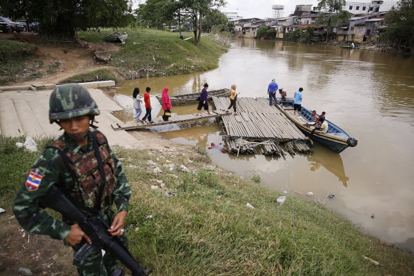 Een soldaat staat op wacht aan de Thaise kant van de rivier terwijl mensen zich klaarmaken om de grens met Maleisië over te steken.