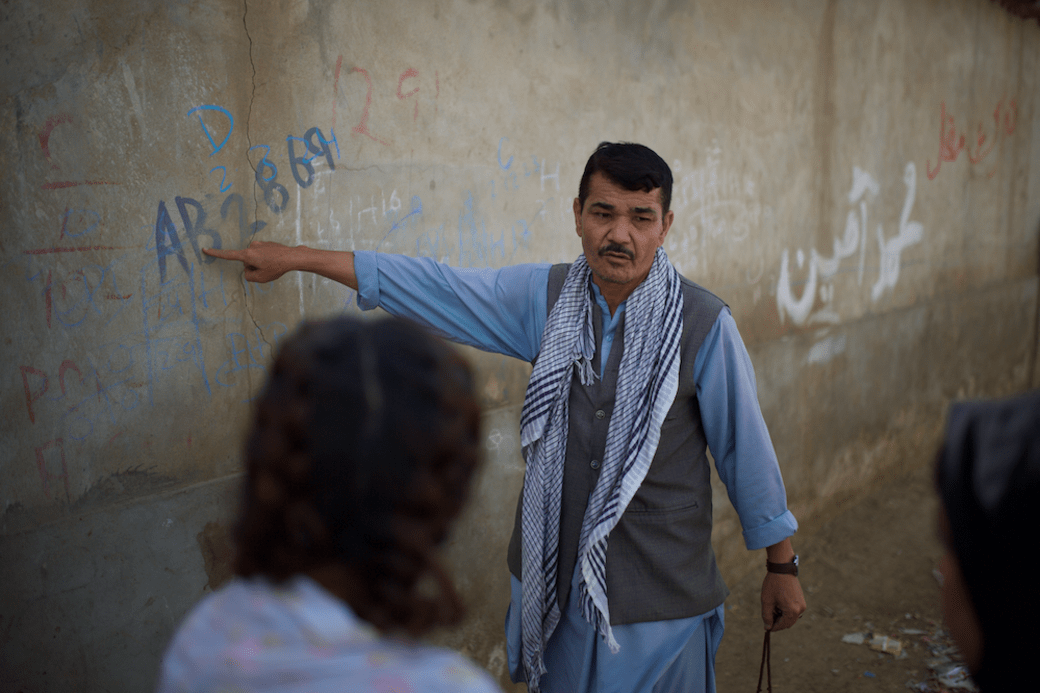 Kampleider Amandula toont de graffiti waarmee de Pakistaanse politie alle huizen in het vluchtelingenkamp heeft gemarkeerd om de verblijfsstatus van de bewoners aan te geven. Dat om de deportaties te vergemakkelijken.
