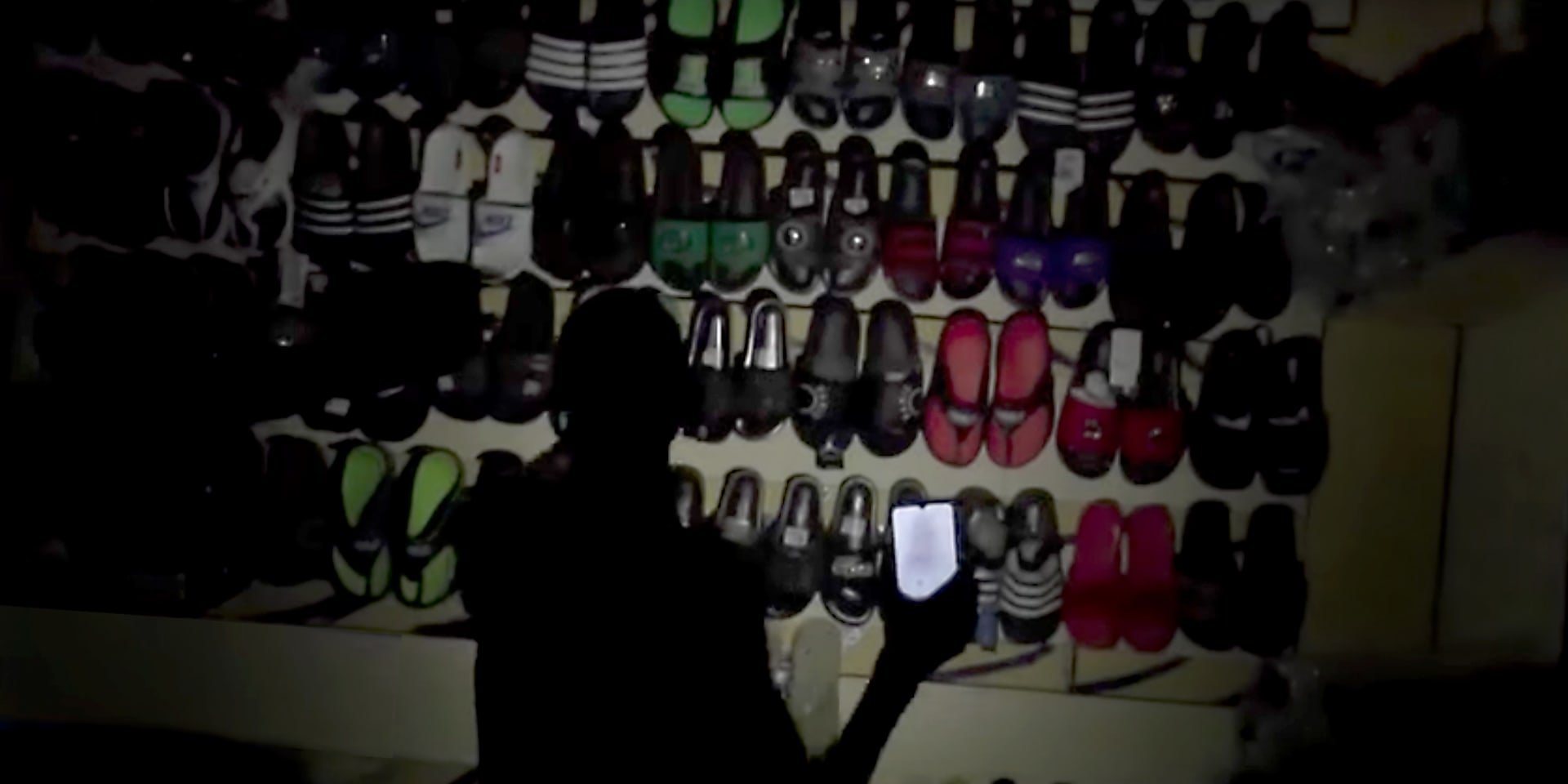 Een man kijkt tijdens een stroompanne naar slippers op een markt in Mali.