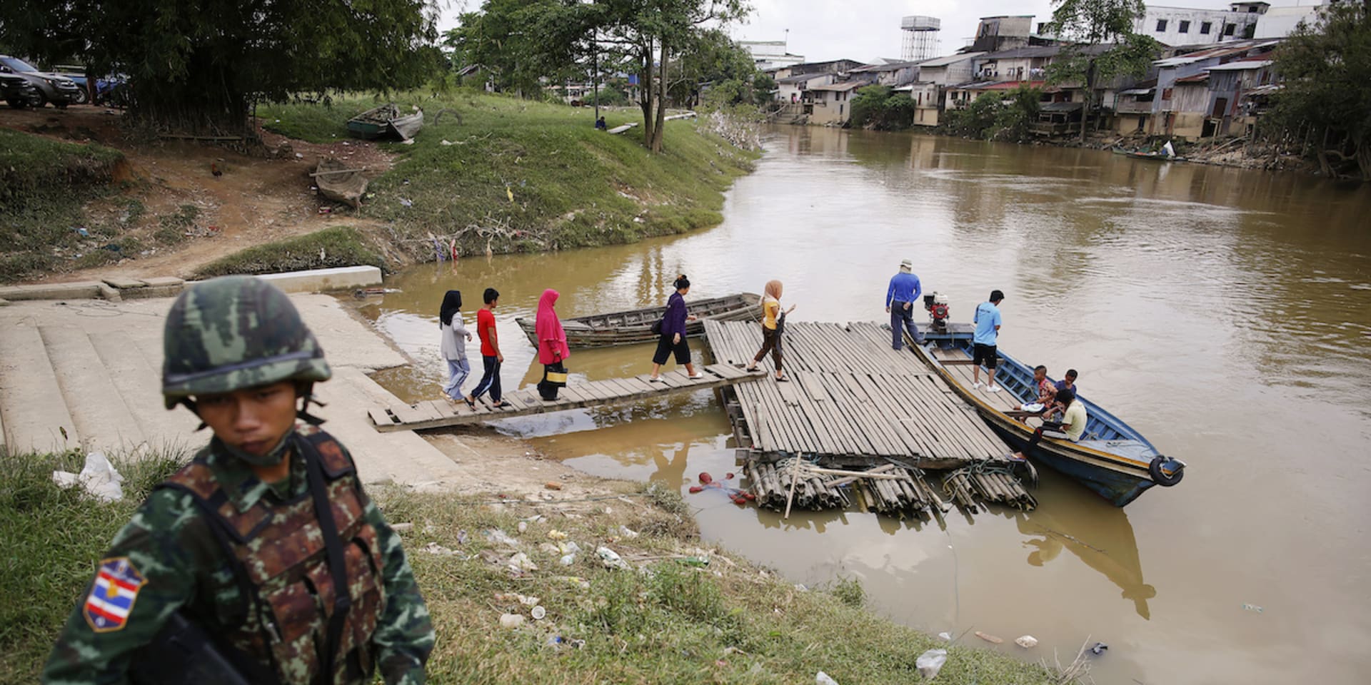 Een soldaat staat op wacht aan de Thaise kant van de rivier terwijl mensen zich klaarmaken om de grens met Maleisië over te steken.