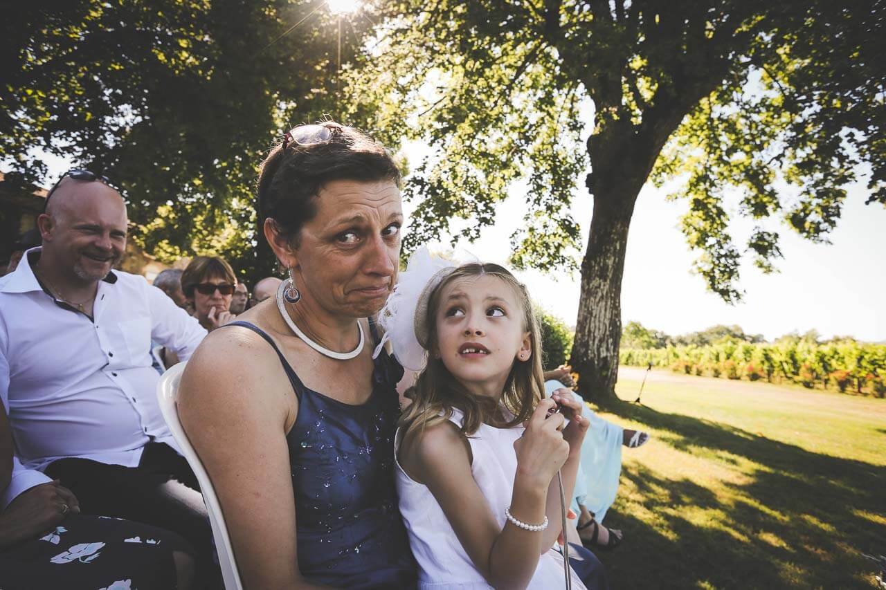 Une maman qui retient ses larmes devant l’objectif avec sa petite fille et son cousin derrière qui rigole