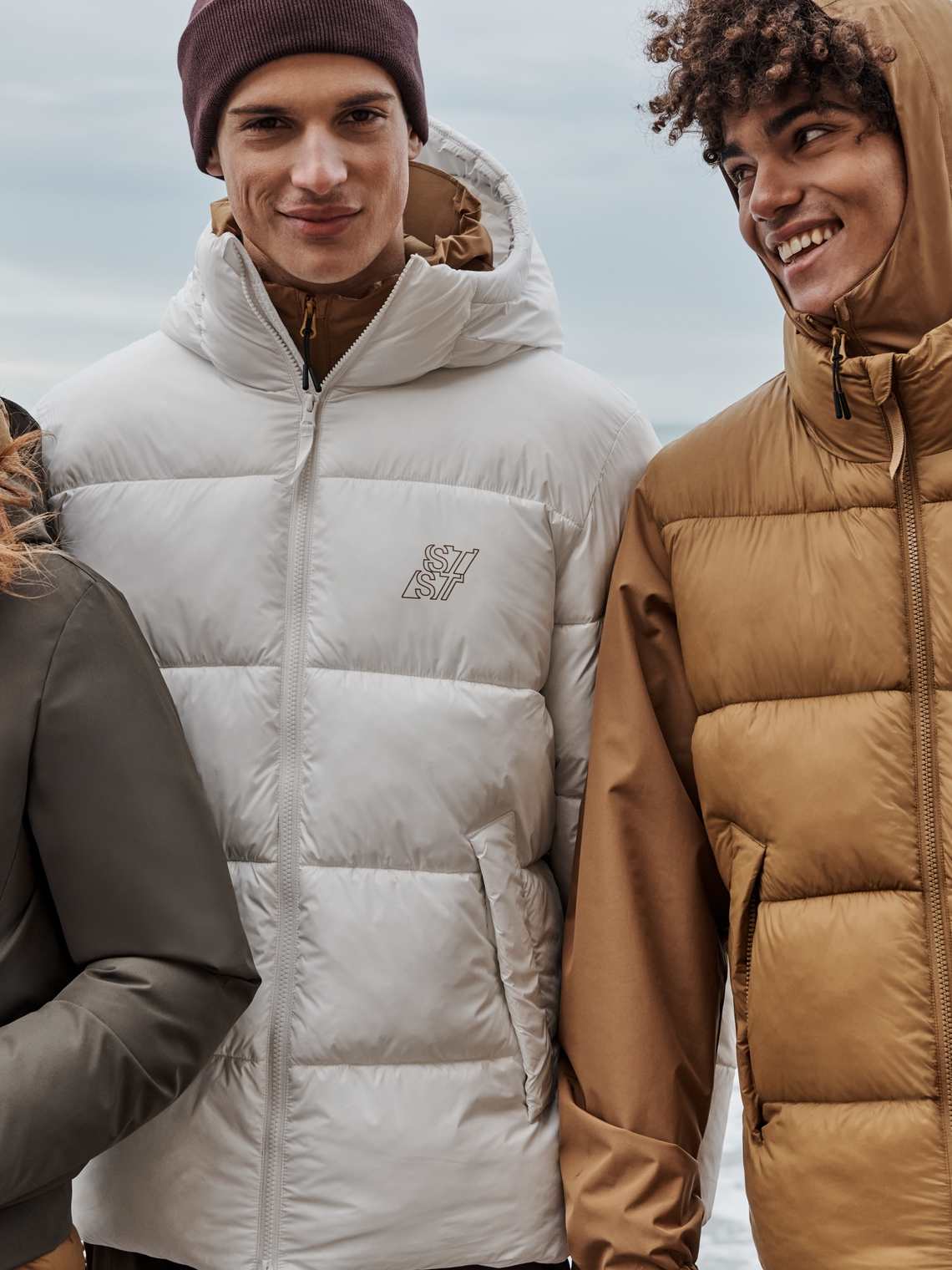 Groepsfoto's AW26 outerwear: donsjassen en regenjassen aan de kust