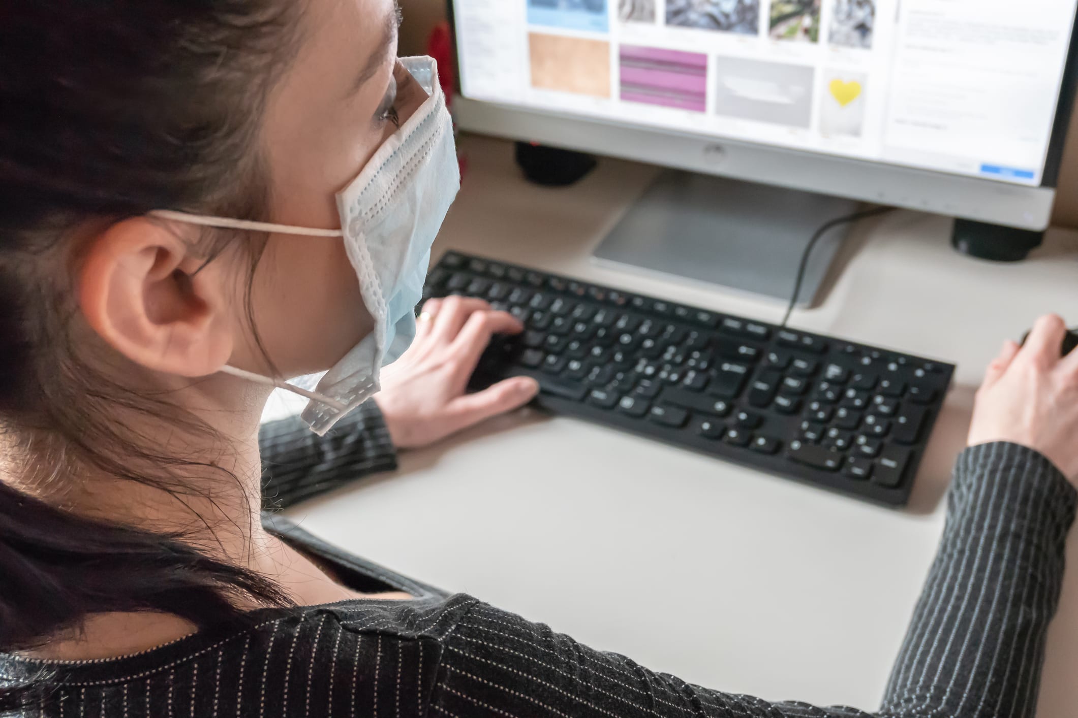 A woman working on a computer while wearing a face mask A woman working on a computer while wearing a face mask