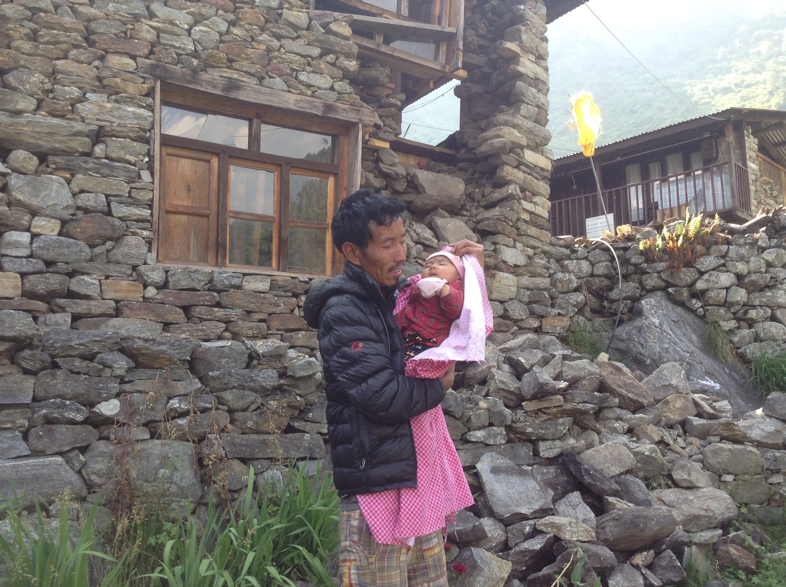 Dawa with his infant daughter stands in front of his damaged house