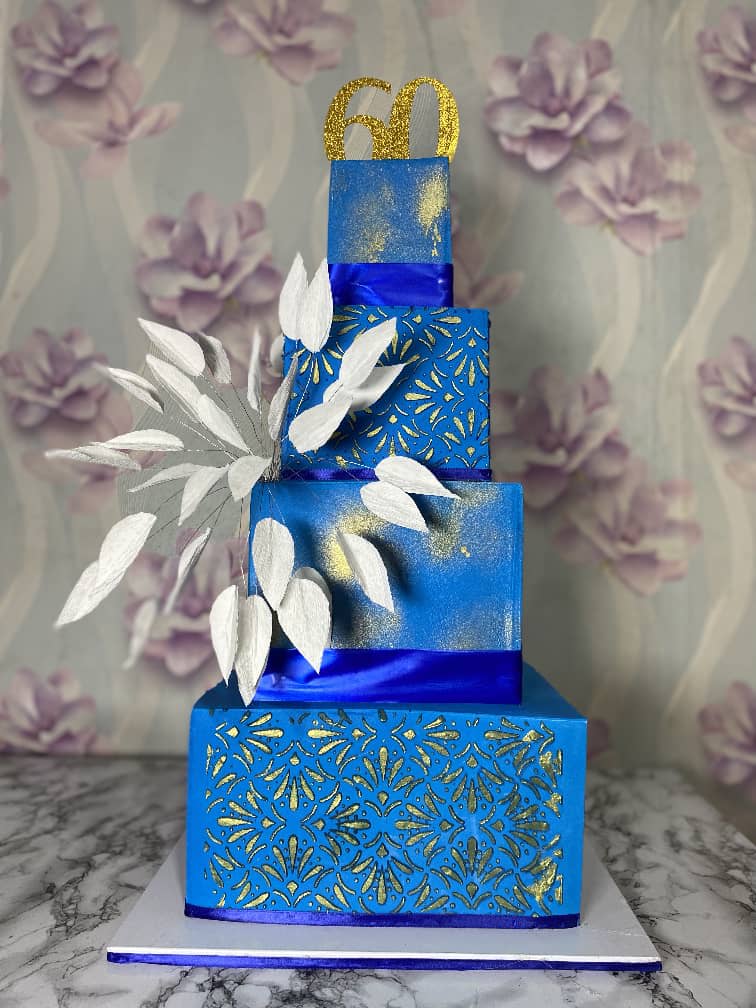 Four-tier square royal-blue cake with gold stencilling, white sugar leaves and a gold 60 topper