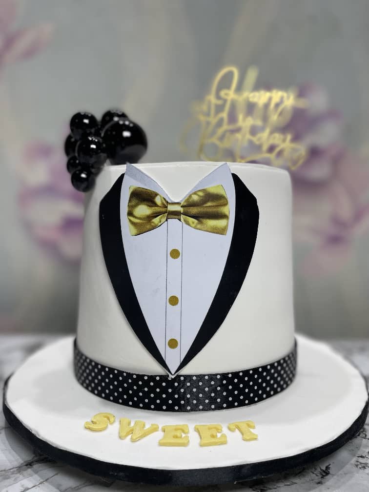 White fondant cake with a tuxedo front, a gold bow tie and buttons, black spheres and a polka-dot ribbon