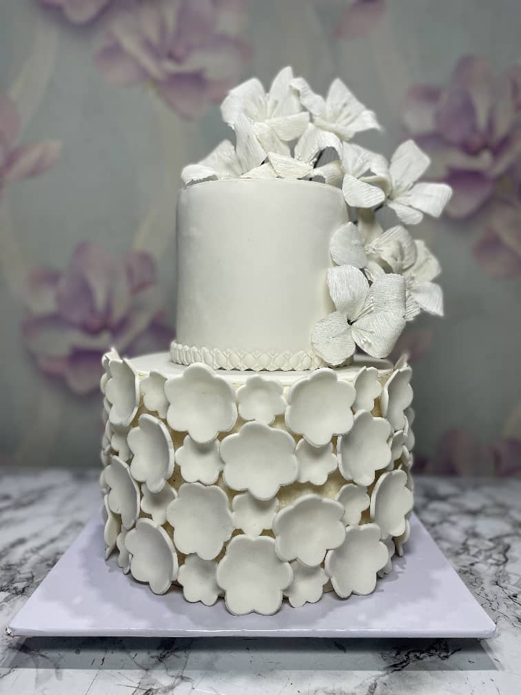 Two-tier white cake covered in white fondant blossoms with white sugar flowers on top