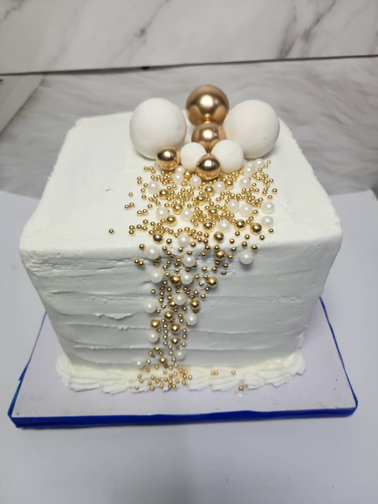 Square white cake with white and gold spheres and a cascade of gold and pearl dragées