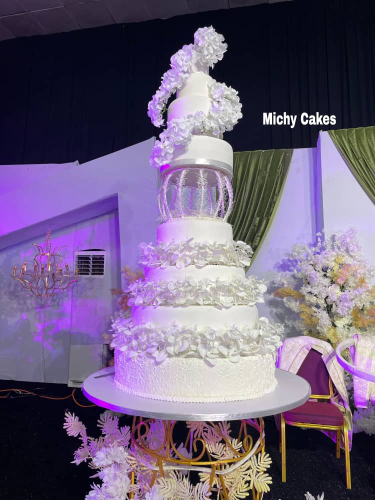 Towering white wedding cake with cascading white hydrangeas, a birdcage tier and tiers trimmed with sugar leaves