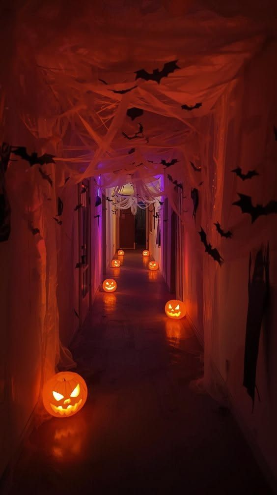 Dark hallway lit in orange for Halloween with glowing pumpkins on the floor and bats hanging overhead