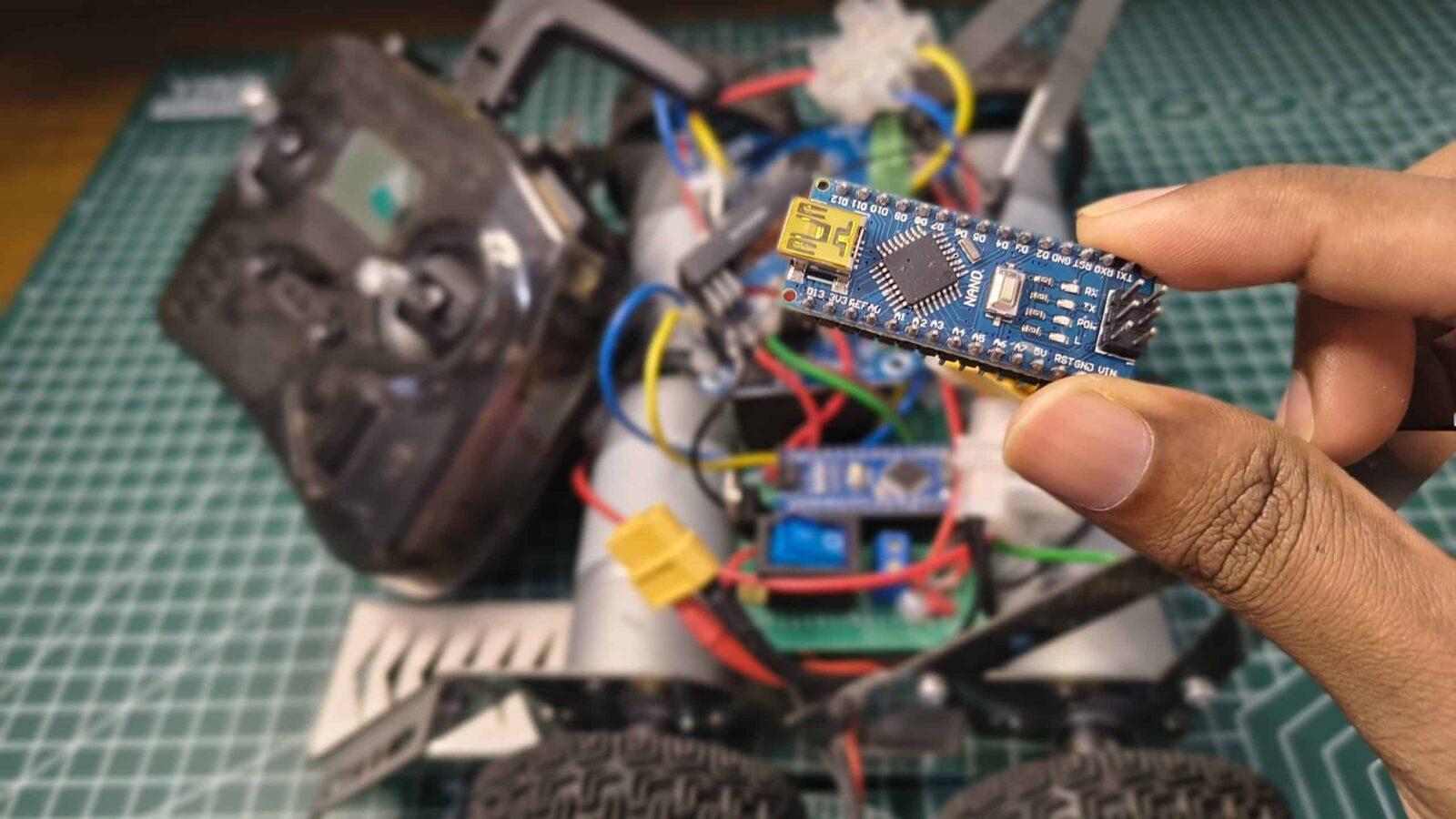 An Arduino Nano microcontroller held in front of a custom 600RPM soccer robot build with a RadioMaster Pocket transmitter in the background.