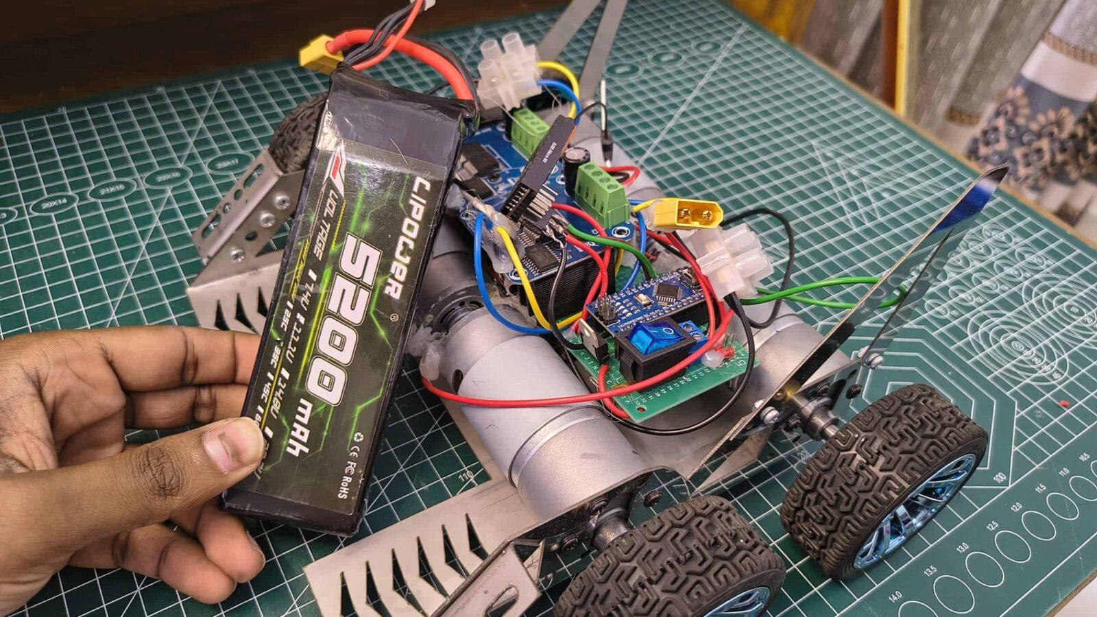 A 5200mAh LiPo battery being installed on a high-speed soccer robot build featuring dual motor drivers and a custom chassis on a green cutting mat.
