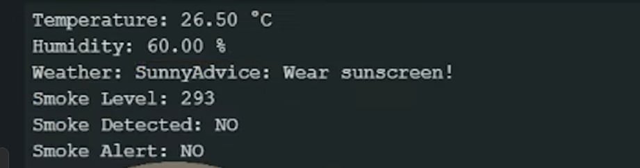 A digital readout from a diy weather station project showing environmental data. The text on a dark background displays a temperature of 26.50°C, humidity at 60.00%, weather as "Sunny," and an advice note saying "Wear sunscreen!". Below this, it lists a smoke level of 293 with "Smoke Detected: NO" a