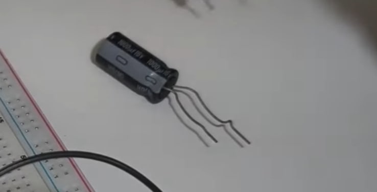 A close-up shot of an electrolytic capacitor with bent leads next to a white breadboard, ready for an electronics breadboard tutorial.