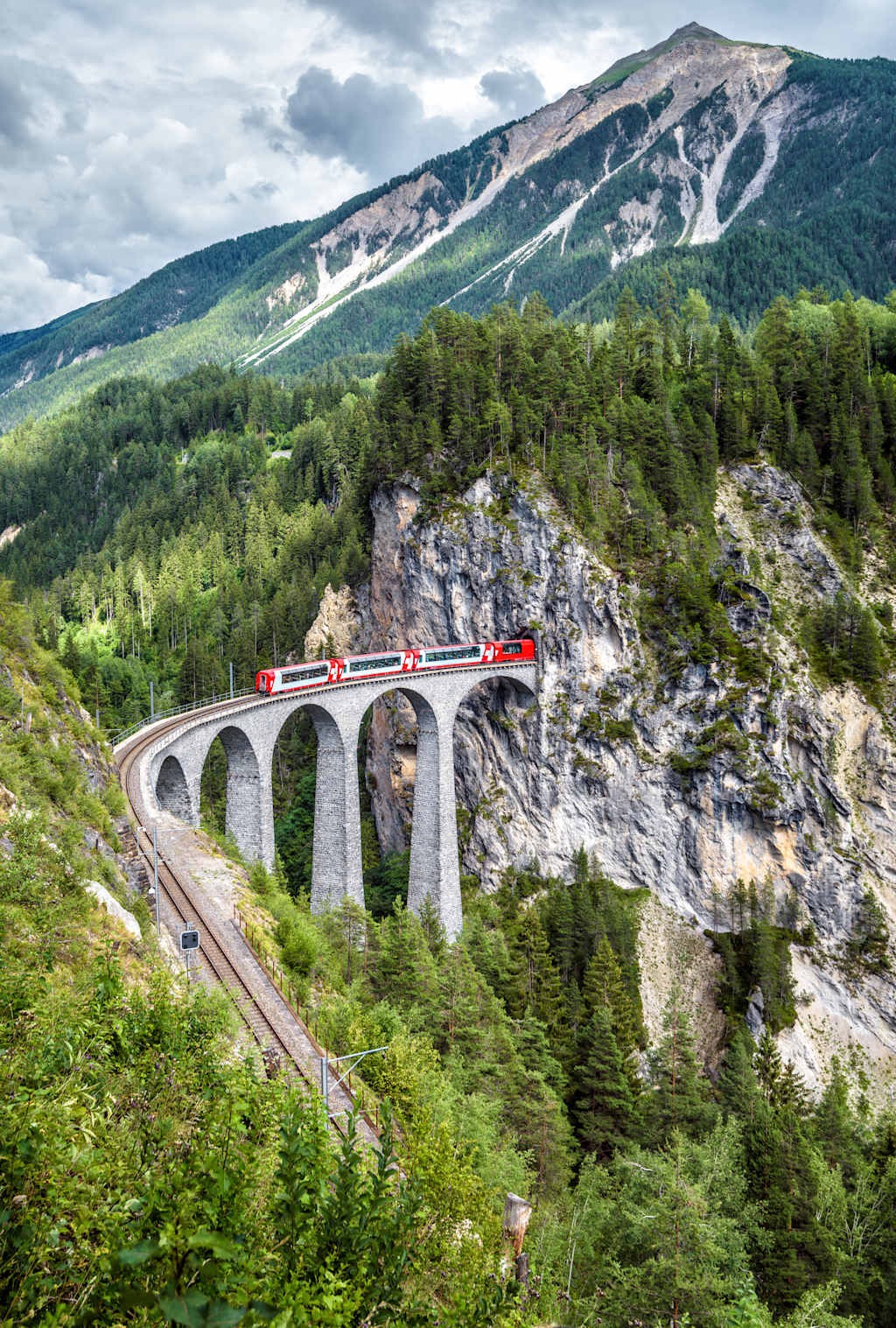 Landwasser Viaduct in summer, Filisur, Switzerland. It is landmark of Swiss Alps. Scenic view of railroad bridge and red train. Alpine landscape with Rhaetian express running on mountain railway.