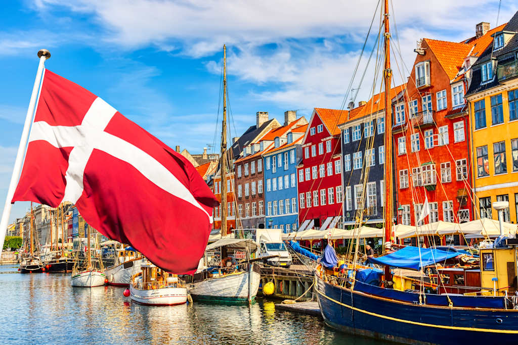 Copenhagen iconic view. Famous old Nyhavn port in the center of Copenhagen, Denmark during summer sunny day with Denmark flag on the foreground