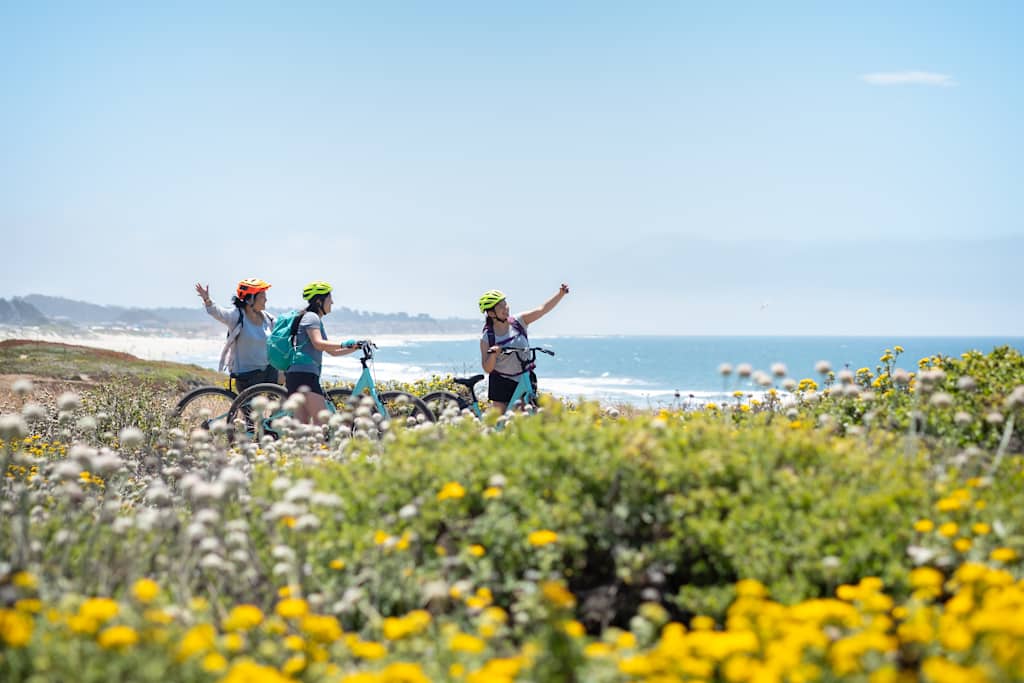 Public biking path in Half Moon Bay, California, USA.  Asian mother with mixed-ethnic millennial daughters pose for selfie while riding rental bikes through wildflower meadows.  Ocean surf and beaches in the background.

CreativeContentBrief 686998871:  Happiness in Nature
CreativeContentBrief 775163423:  Non-Caucasian Travelers