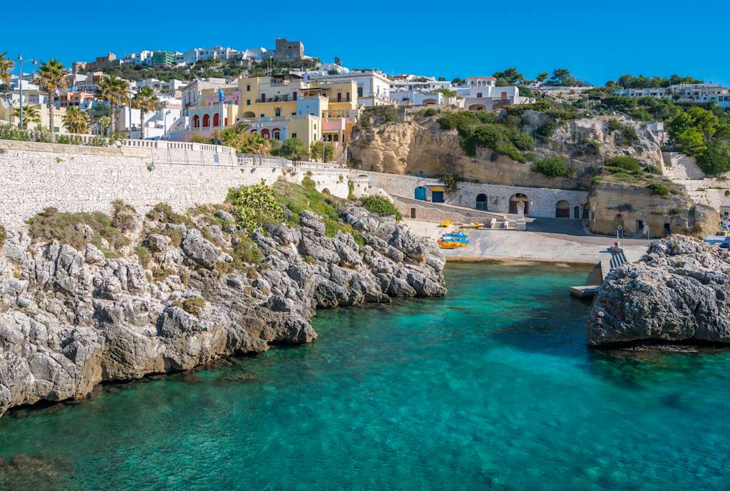 A picturesque coastal town nestled on rocky cliffs, with vibrant white and colorful buildings overlooking a stunning turquoise bay.