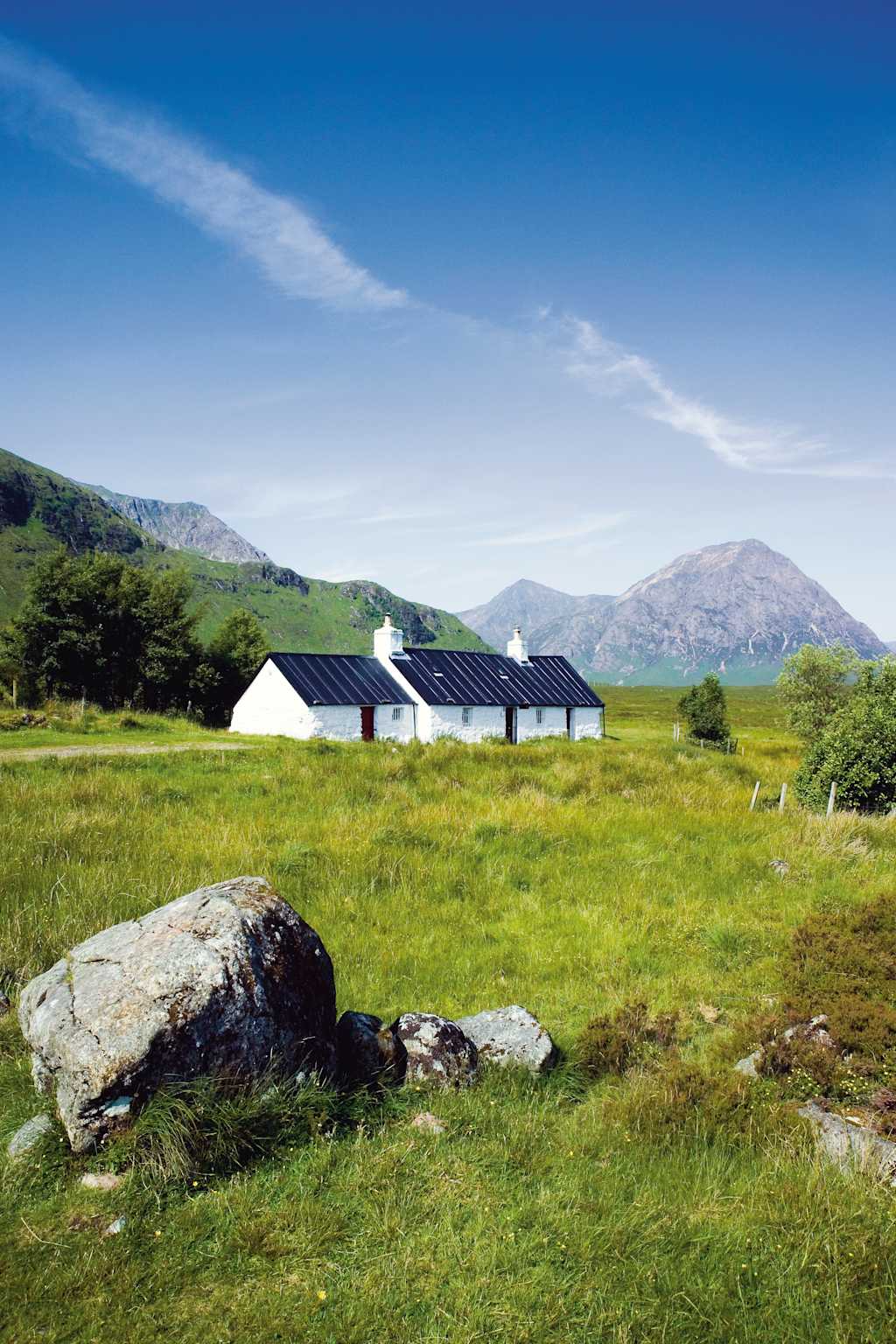 A picturesque rural landscape with a cluster of white cottages nestled amidst a lush green meadow, surrounded by rolling hills and a clear blue sky dotted with wispy clouds.