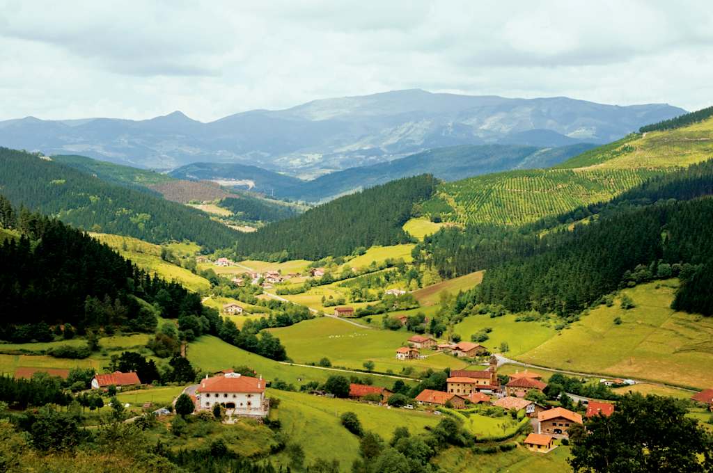 A picturesque mountain valley with lush green hills, forests, and scattered rural settlements nestled among the peaks in the distance.