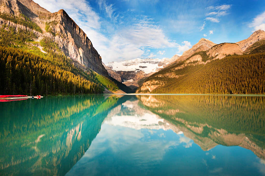A serene alpine lake surrounded by towering mountains, with a reflection of the landscape mirrored perfectly in the still waters, and a small red boat in the foreground.