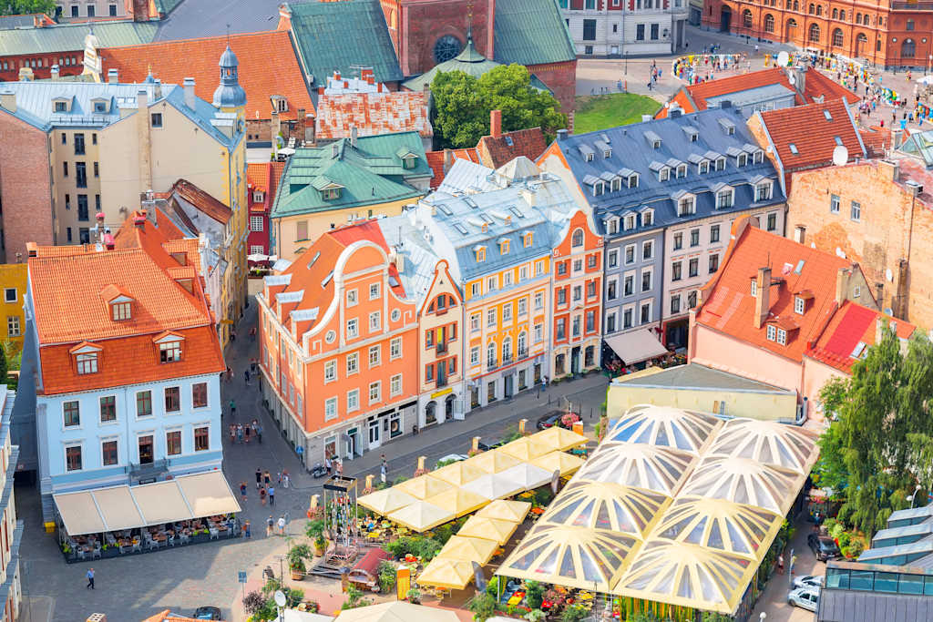 A vibrant cityscape with colorful, historic buildings, bustling streets, and a large, distinctive tent-like structure in the foreground, creating a lively and visually captivating scene.