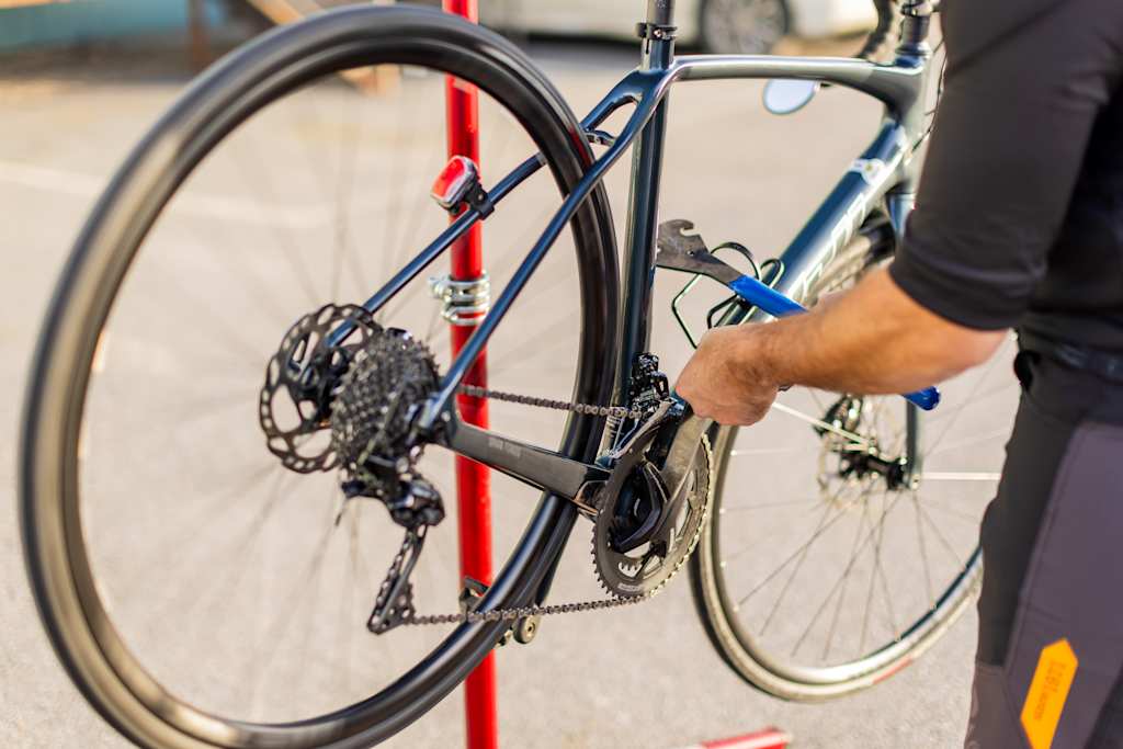 A close-up view of a person's hand adjusting the rear derailleur on a bicycle, with the bicycle's frame and wheels visible in the background.