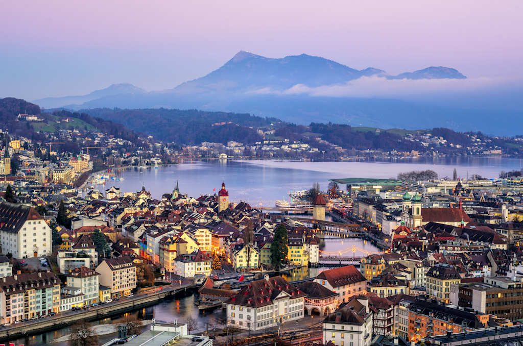 A picturesque cityscape nestled along a lake, with colorful buildings and a majestic mountain range rising in the background, creating a breathtaking landscape.