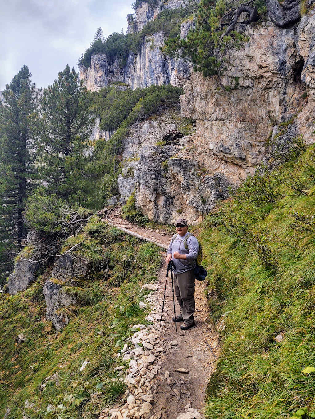 A person is walking along a rocky, winding trail surrounded by lush greenery and towering cliffs in the background.