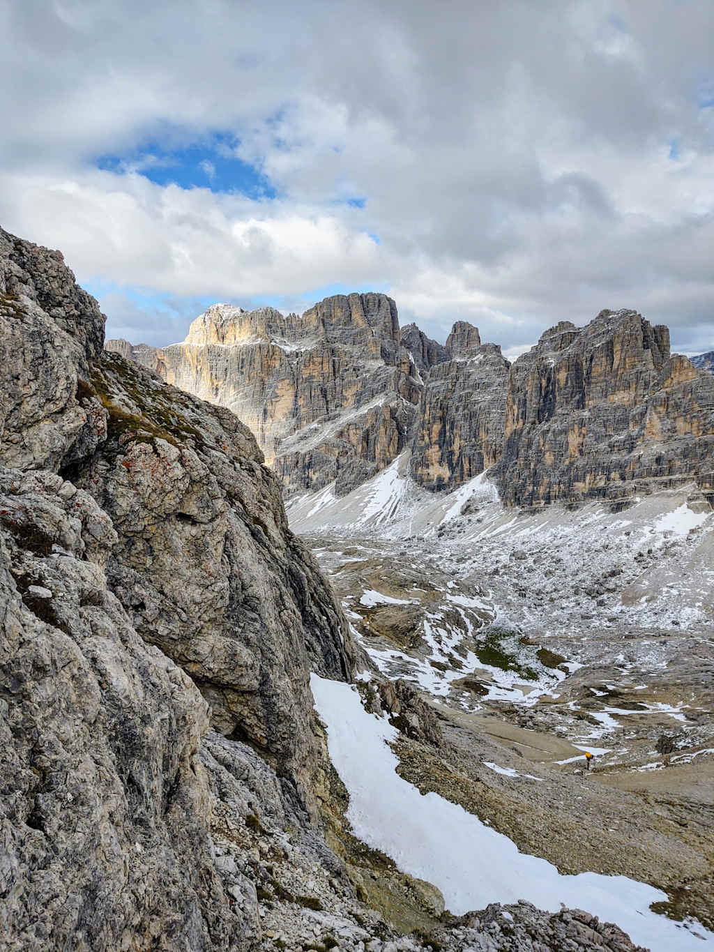 Rugged, snow-capped mountains rise majestically in the background, while the foreground features a rocky, snow-covered landscape with a small stream winding through it.