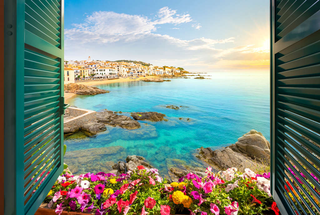 A picturesque coastal town with colorful houses, surrounded by a tranquil turquoise sea and framed by vibrant flowers in the foreground.