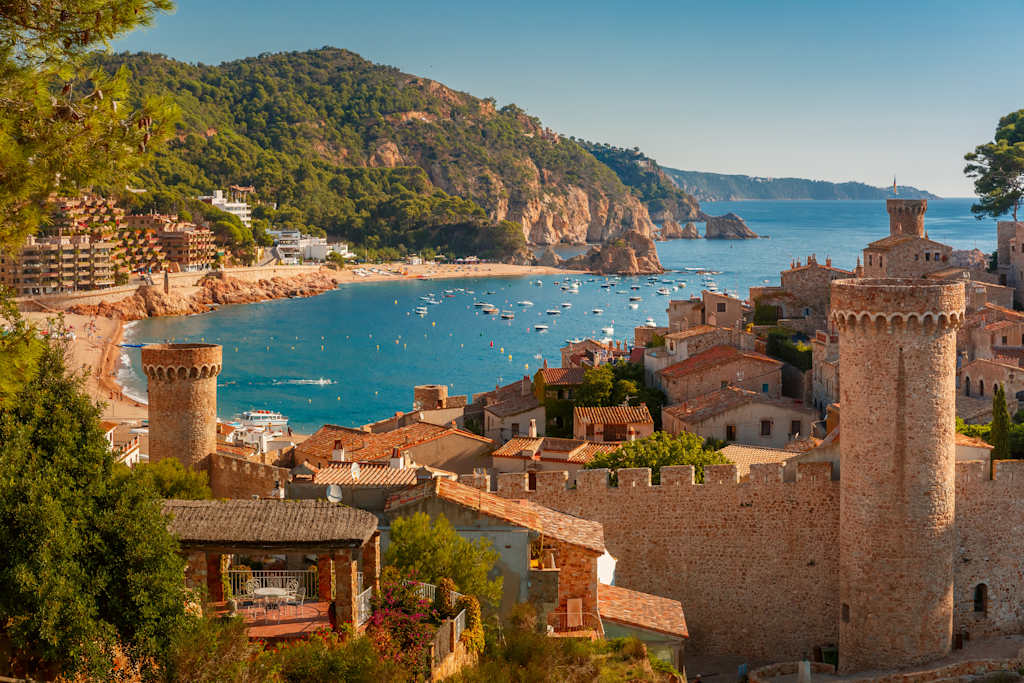 A picturesque coastal town nestled between rugged mountains, with a vibrant harbor filled with boats and surrounded by historic buildings and towers.