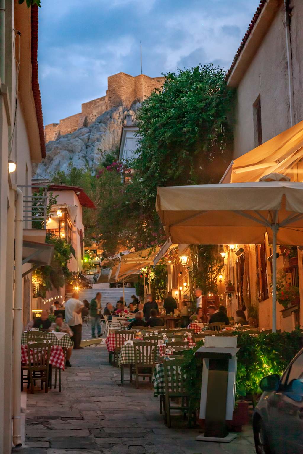 A cozy outdoor dining area with tables and chairs, surrounded by colorful buildings, lush greenery, and a towering rock formation in the background, creating a charming and inviting atmosphere.
