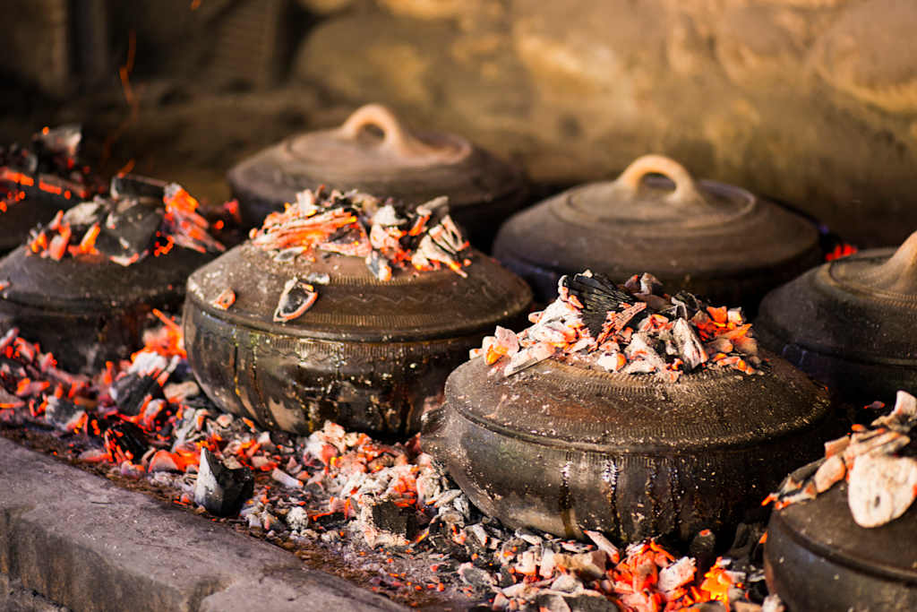 Rustic clay pots sit amidst glowing embers and scattered petals, creating a warm and earthy scene.