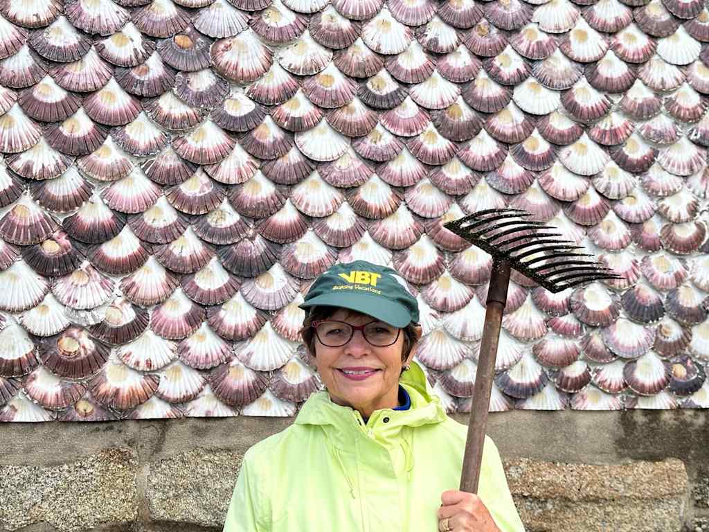 A person wearing a green cap and a bright yellow jacket stands in front of a wall covered in iridescent seashell-like patterns.