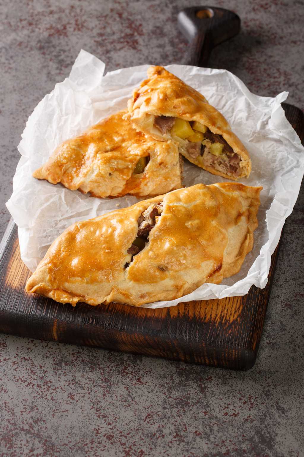 A wooden cutting board holds two slices of what appears to be a savory pastry or calzone, filled with ingredients and baked to a golden brown.