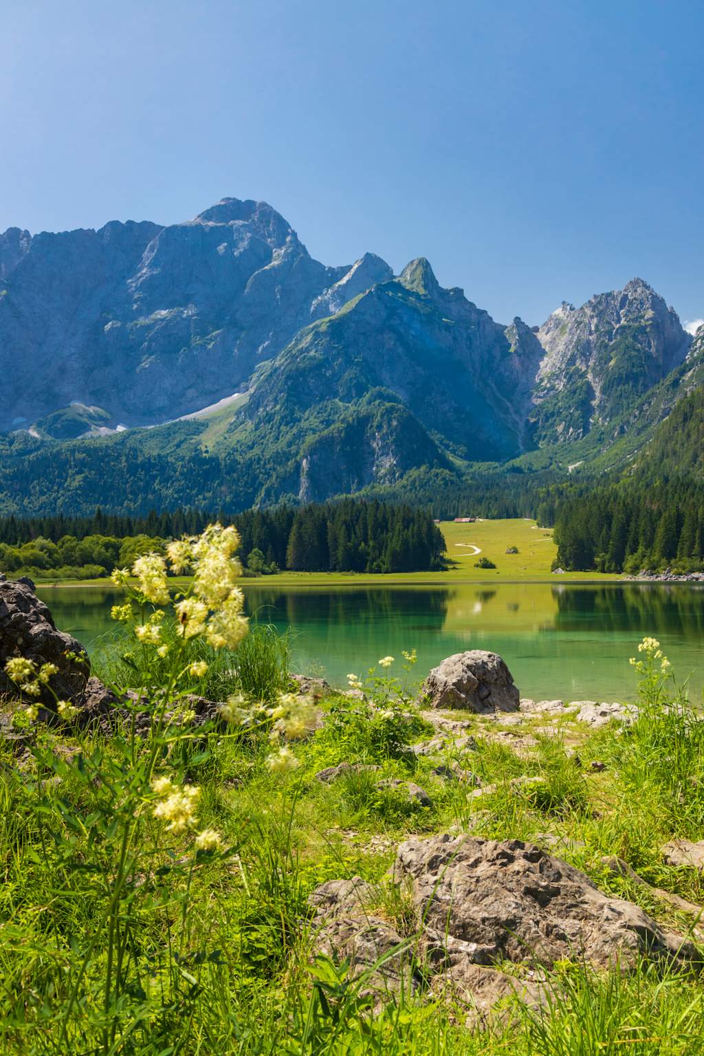A serene mountain lake surrounded by lush green vegetation and towering peaks in the background, creating a picturesque natural landscape.