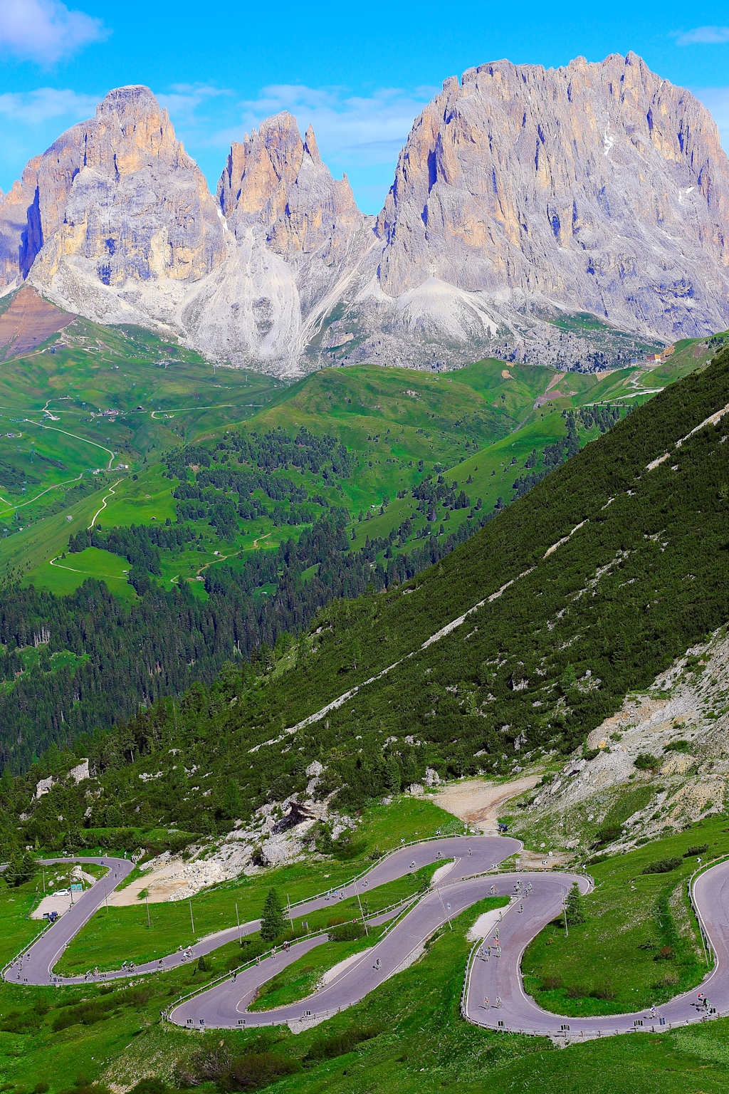 Majestic snow-capped mountains rise in the background, while a winding road cuts through the lush, verdant landscape in the foreground.