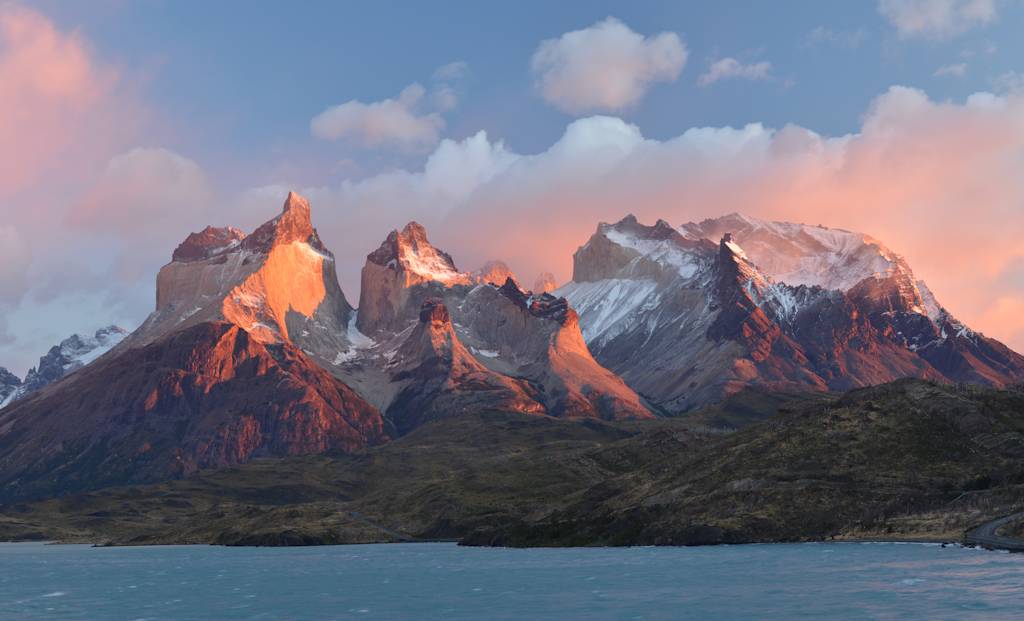 Majestic snow-capped mountains rise against a vibrant sky, reflected in the serene waters of the foreground lake, creating a breathtaking natural landscape.