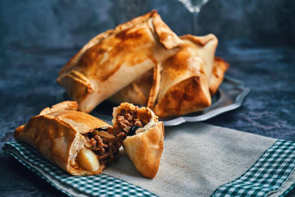 Freshly baked pastries with a flaky crust and a savory filling, resting on a checkered cloth against a dark background.