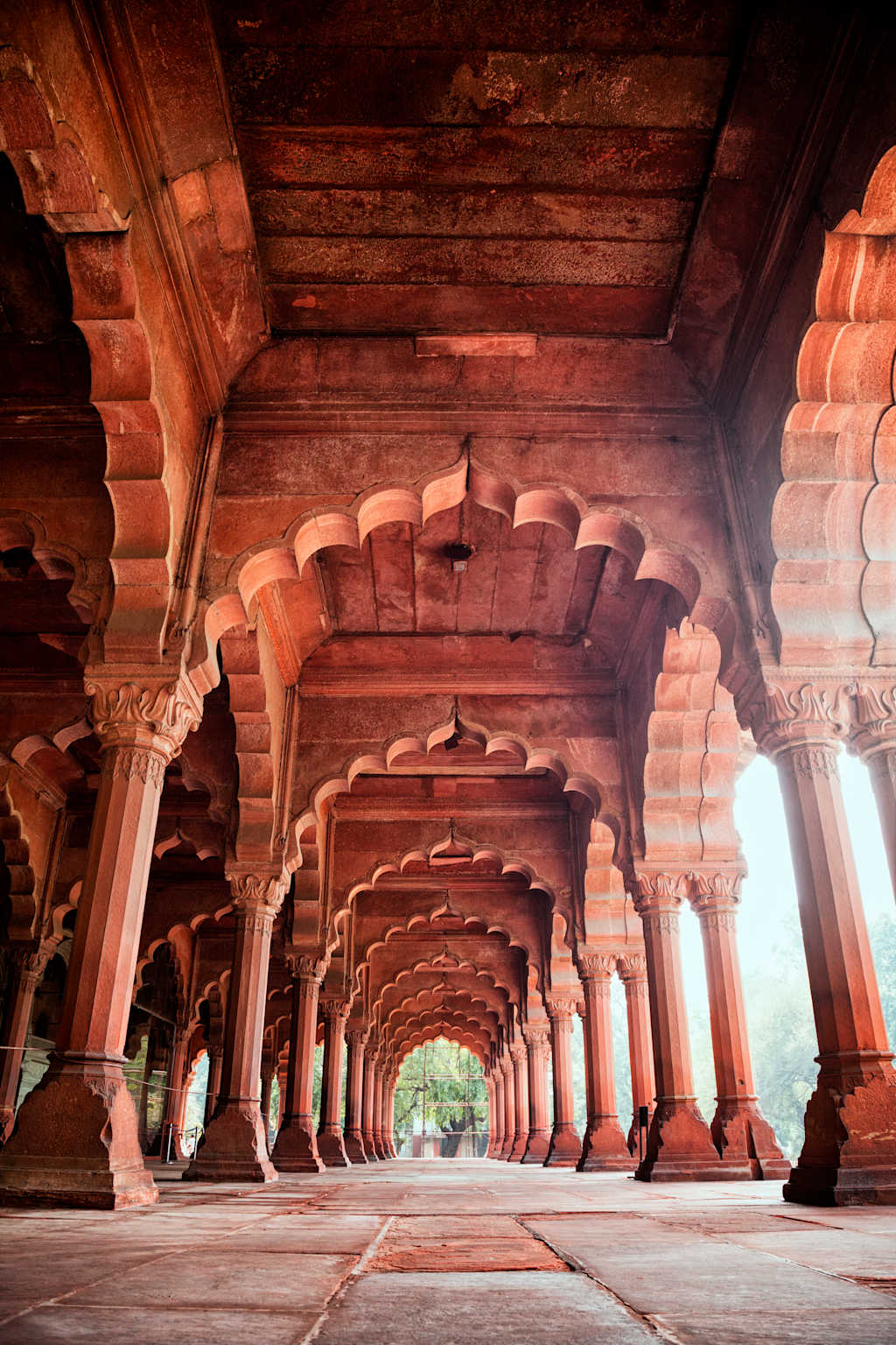 A grand, ornate archway with intricate carvings and columns leading to a lush, verdant outdoor space beyond.
